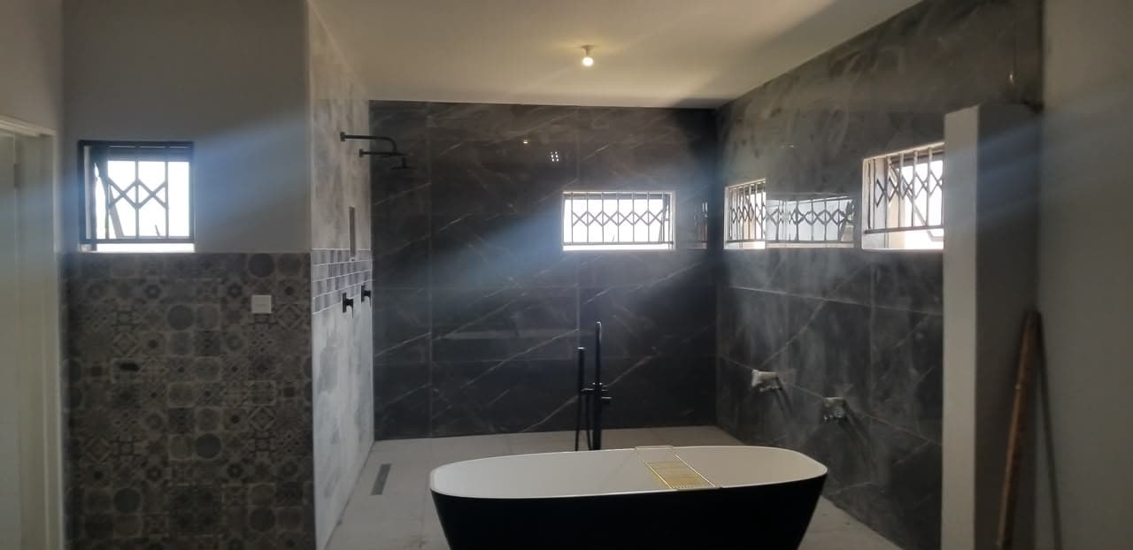 Master bathroom tiled in dark marble with a black freestanding bath, matte black mixer and a walk-in shower with a linear drain