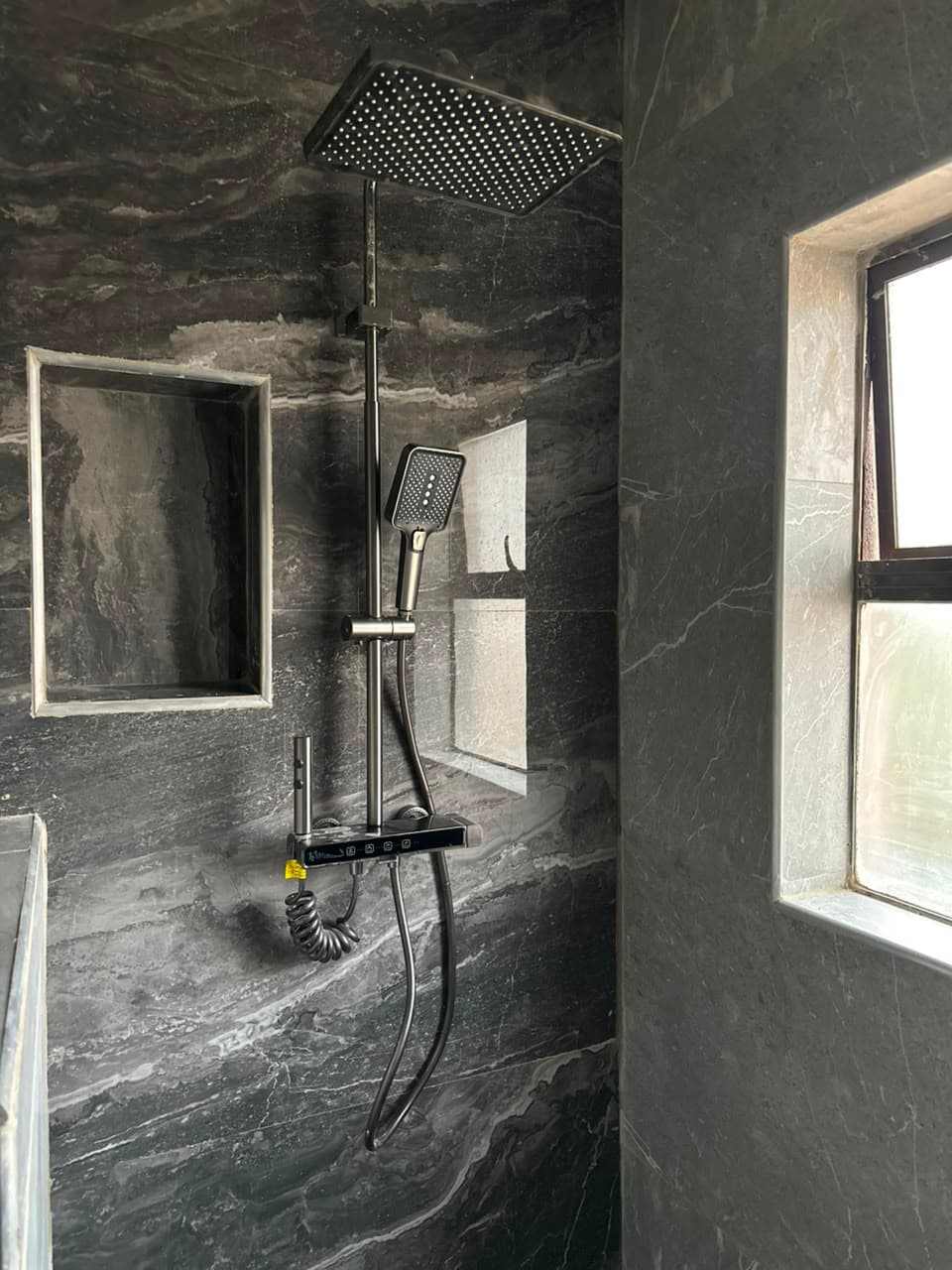 Black thermostatic shower column with a slimline rain head and a recessed tiled niche, on dark marble-effect porcelain