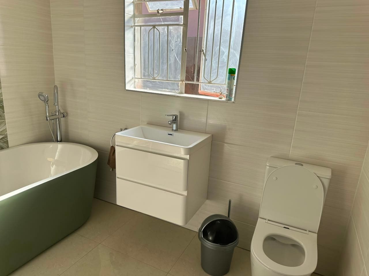 Completed family bathroom with an olive green freestanding bath, a gloss wall-hung vanity unit and a close-coupled toilet