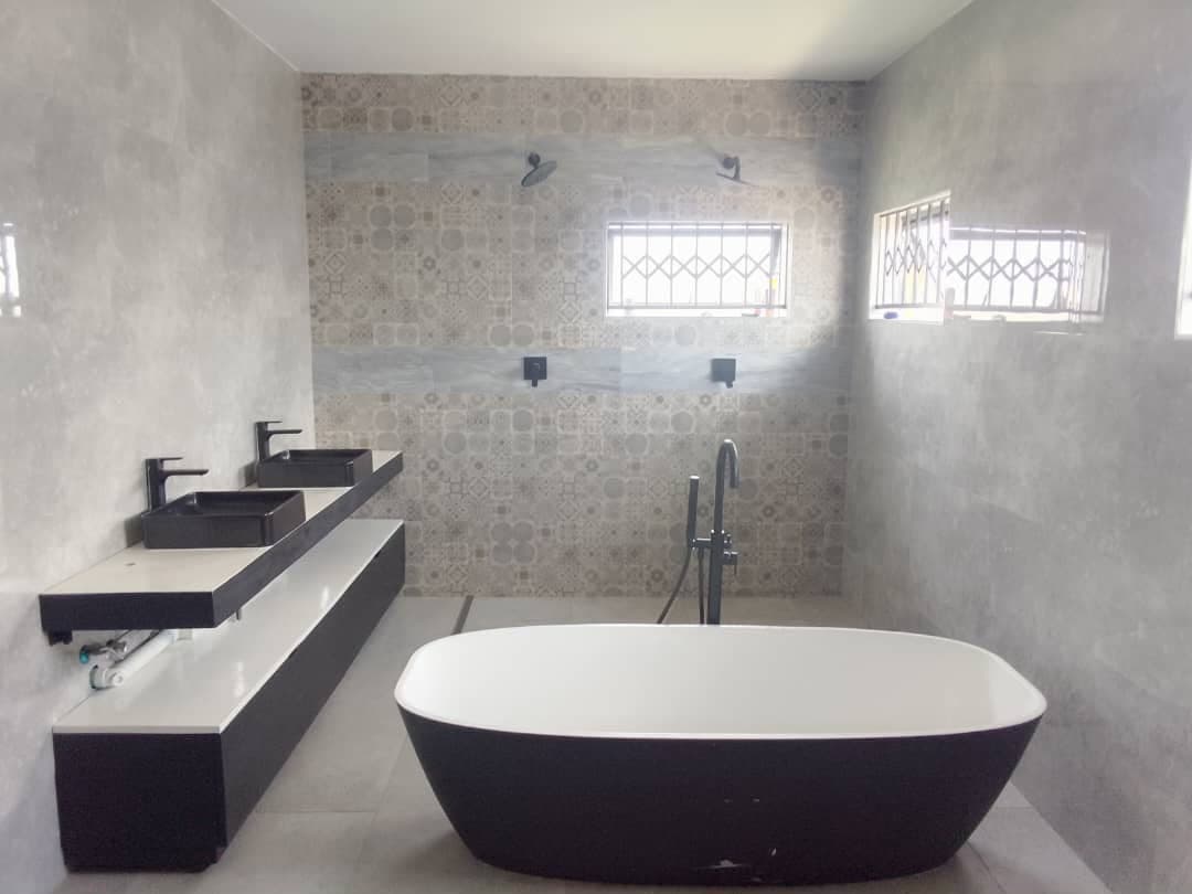 Long wall-hung vanity carrying two black counter-top basins, facing a freestanding bath and a twin-head walk-in shower