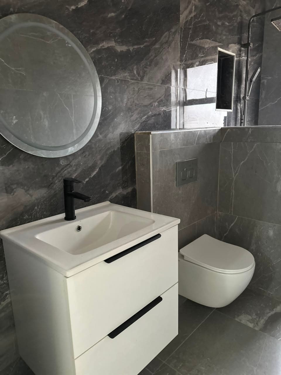 En-suite with a wall-hung vanity, a round backlit mirror and a wall-hung toilet on a concealed cistern with a chrome flush plate