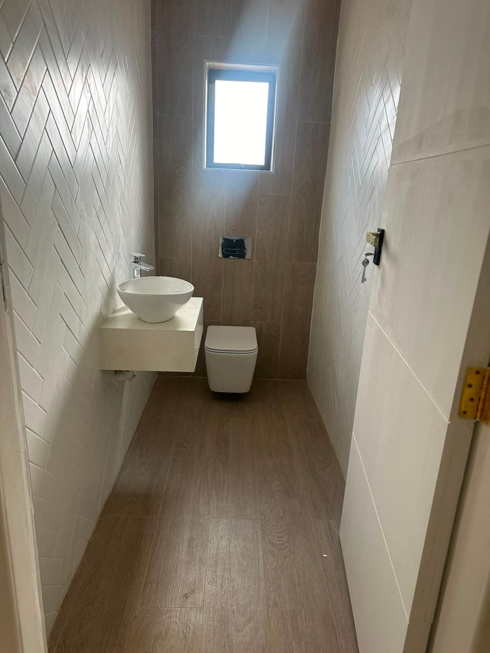 Compact guest cloakroom with herringbone wall tiling, a wall-hung toilet on a concealed cistern and a counter-top basin on a floating shelf