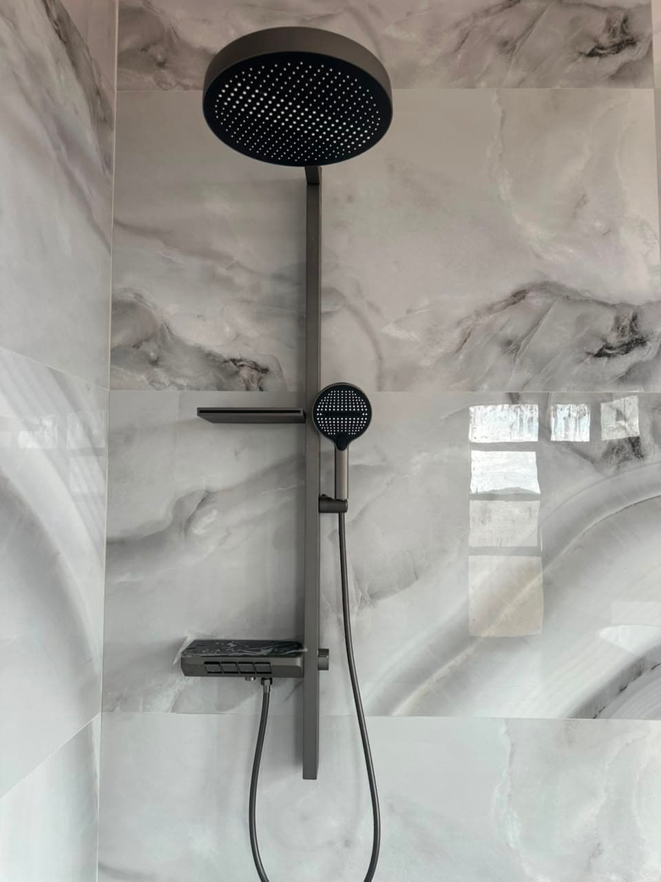 Gunmetal rain shower column with a push-button thermostatic bar and handheld, mounted on white marble-effect porcelain