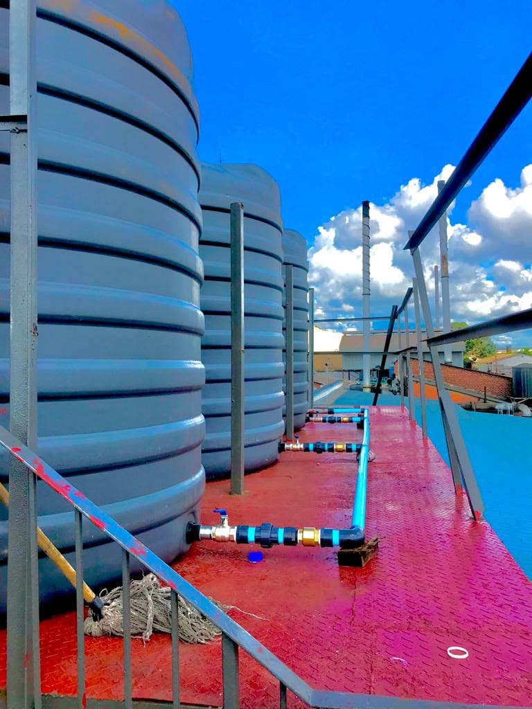 Three water storage tanks on a steel roof platform, linked by a blue PPR manifold with isolating valves at each tank