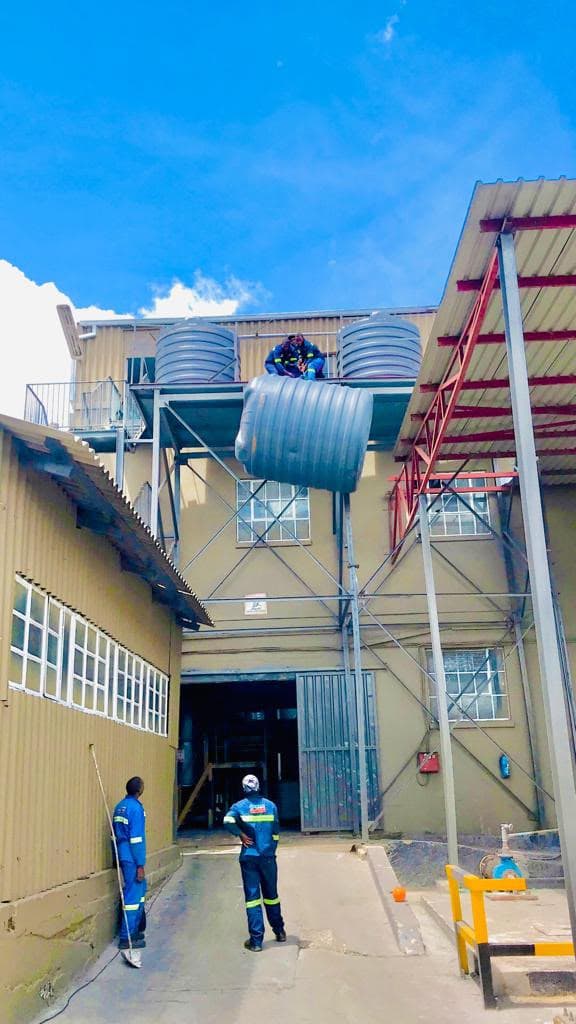 Crew positioning a bank of water storage tanks on a raised steel stand at a commercial premises