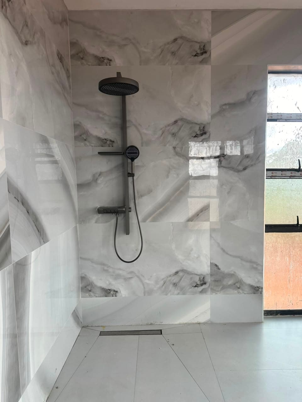 Open walk-in shower in white marble-effect porcelain with a gunmetal rain head and a linear floor drain